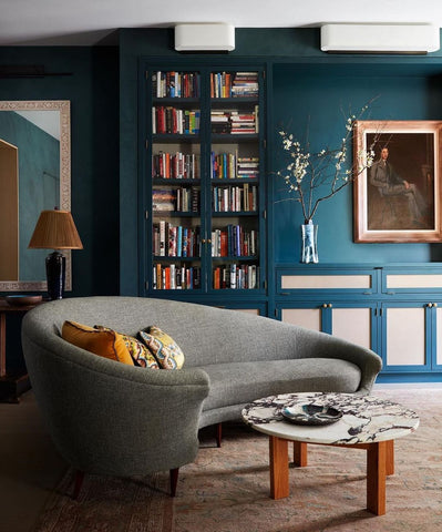 Teal walls with white accents, bookshelves and gray couch.