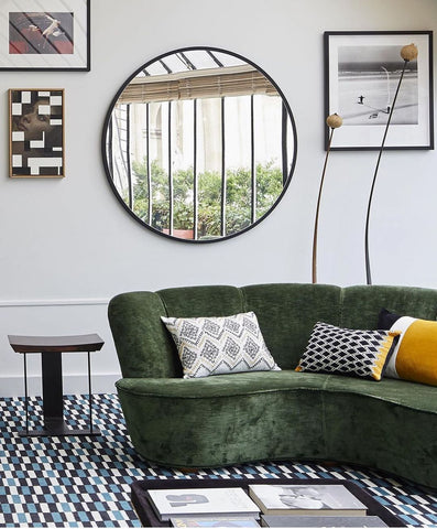 White space with frames and circular mirror on the wall. Green lounge couch.