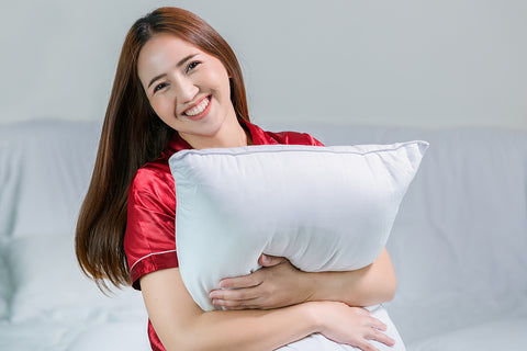 Smiling woman enjoying comfort while gently squeezing a pillow in her arms
