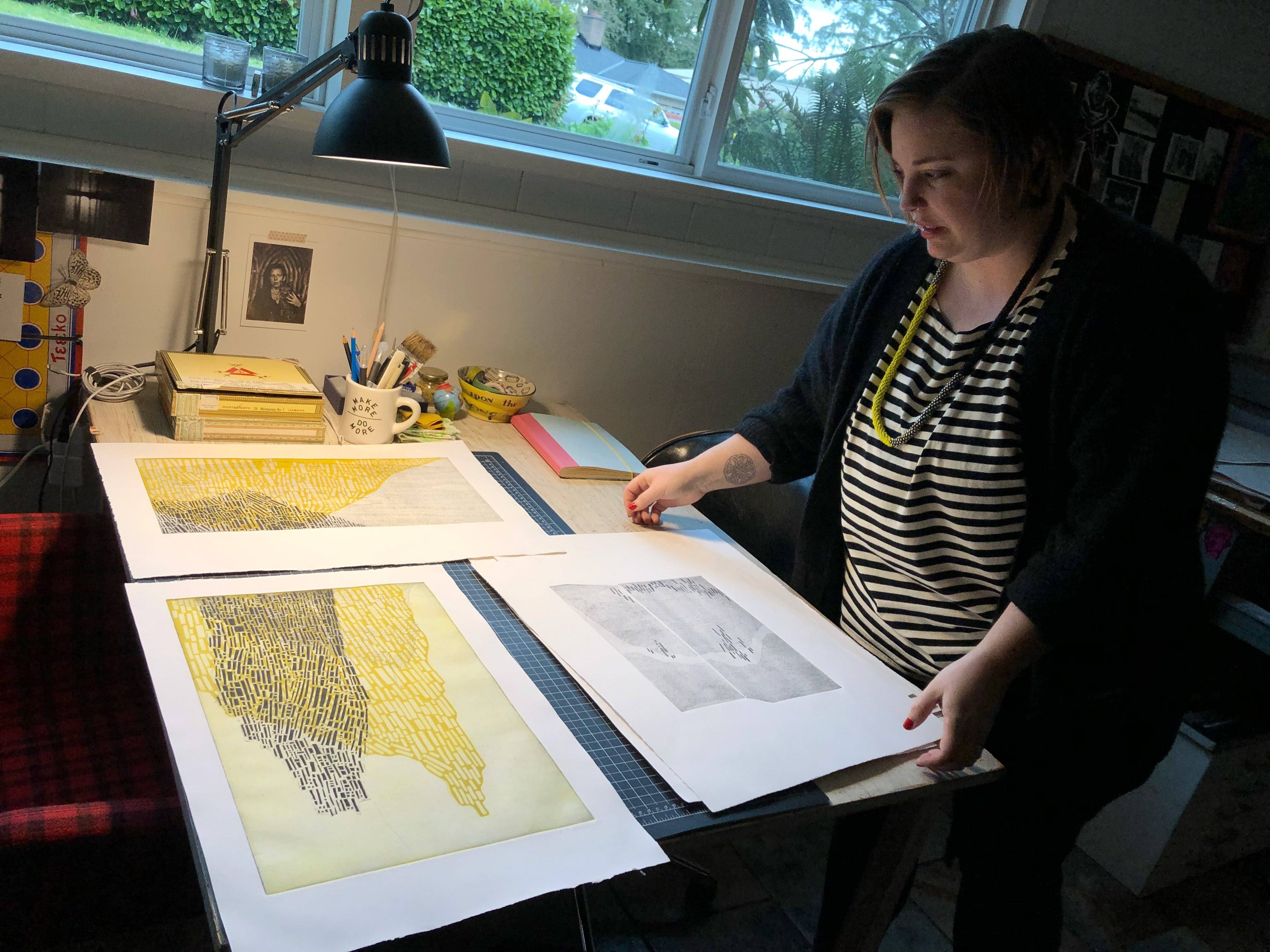 Virginia Hungate-Hawk stands over her work table in her studio, showing her etchings.