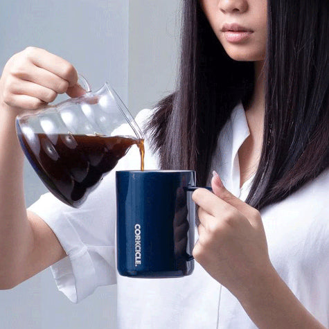 A woman in a white button-up shirt pouring coffee into a custom Corkcicle coffee mug