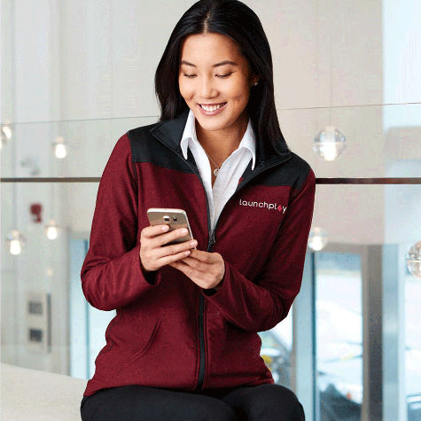 woman texting on cell phone and smiling wearing a maroon corporate Elevate women's layering piece