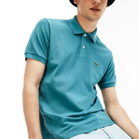 A young man in a teal custom Lacoste men's polo shirt and a hat posing against a white background