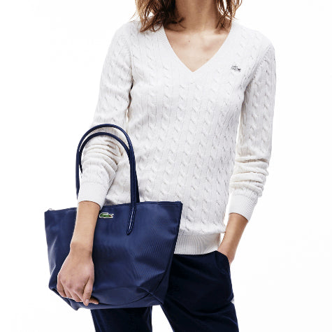 A woman in a custom white Lacoste sweater holding a navy corporate Lacoste tote bag in front of a white background