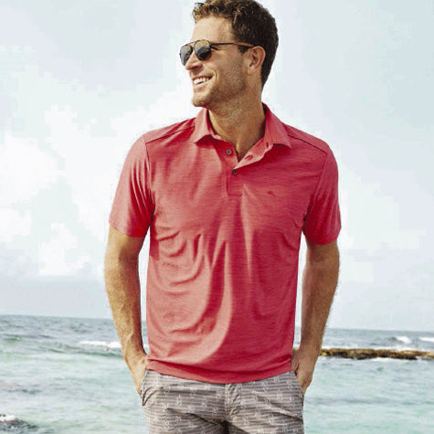 A man walking on the beach wearing sunglasses and a pink corporate Tommy Bahama men's polo shirt