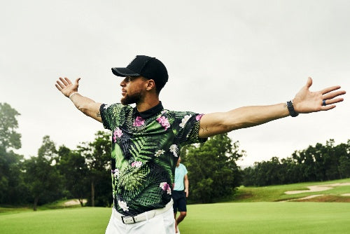 Professional athlete Stephen Curry wearing a corporate Under Armour hat and floral t-shirt on a golf course