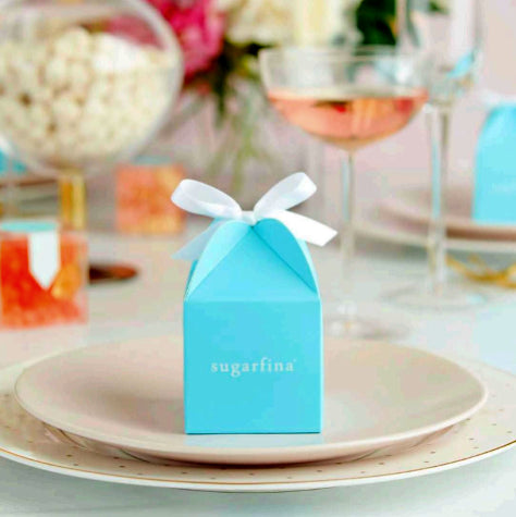 A gorgeous teal custom candy box with a white ribbon tying it shut on a plate in front of a holiday themed table