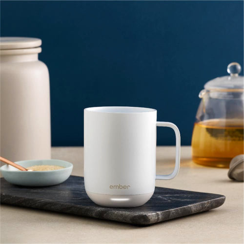 A white corporate Ember smart mug sitting on a countertop with a white ceramic container and a glass honey jar sitting next to it