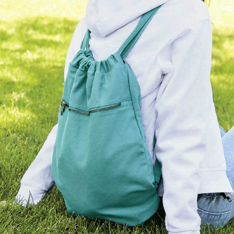 A person sitting on the grass with a teal cinch bag on her back with a custom logo