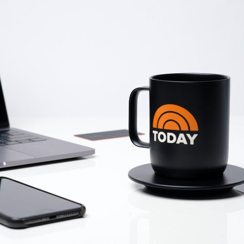 A smartphone, laptop, and a custom logo branded Ember smart mug sit on a white desk