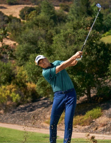 A professional golfer wearing a custom logo branded Under Armour golf polo on a golf course while playing a round of golf