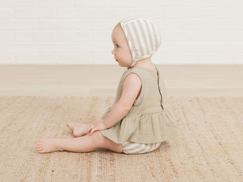 Baby girl sitting up wearing the new Quincy Mae SS21 peplum set in sage stripe and the sage stripe bonnet. 