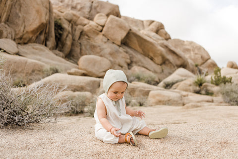 Briar Baby Linen Bonnet in sand on baby on beach with desert rocks behind - lifestyle shot of the bonnet 