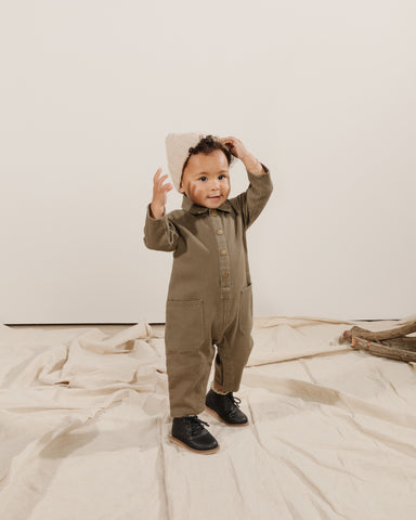 Toddler in a studio wearing boots and the new Rylee + Cru Autumn Winter 2021 Drop 2 Collection Snap Jumpsuit (painter style) in olive with the agave beanie hat. 