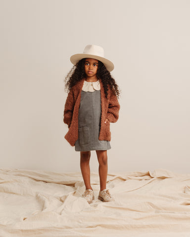 Little girl in a studio shoot wearing the new Rylee + Cru AW21 Drop 2 Odette corduroy overall jumper dress in Indigo with the Oversized Collar Blouse in Stone and the soft longline cardigan in wine. 