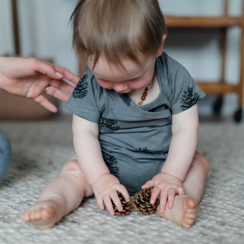 baby wearing Buck and Baa pinecone wrap one piece bodysuit (onesie) with an adult hand reaching out to support him as he sits