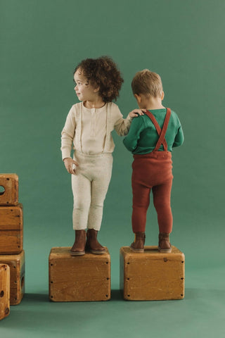 Fin & Vince Chapter 2 - toddlers wearing knit suspender pants and wrap cardigans in confetti and gingerbread standing on suitcases. 