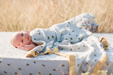 Lifestyle photo of infant baby on new Milkbarn Kids bamboo crib sheet in bumblebee, covered in the Big Lovey in Bumblebee in a wheat field