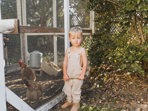 Boy wearing Rylee + Cru striped jumpsuit standing by a chicken coop
