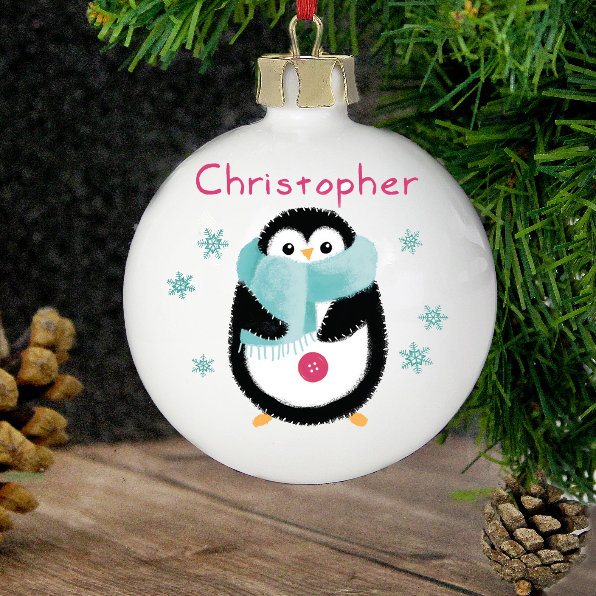 Personalised white ceramic Christmas tree bauble with an illlustration of a hand-drawn penguin on the front wearing a blue scarf and a name of your choice in a red font printed above the penguin. The rear of the bauble can be personalised with your own special message over up to 4 lines.