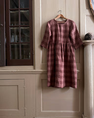 a brown checked linen dress hangs on a old wooden paneled wall