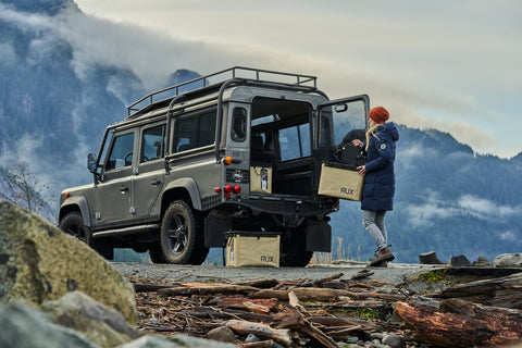 On top of a mountain we see a woman unloading the RUX 70L from the back her Jeep.