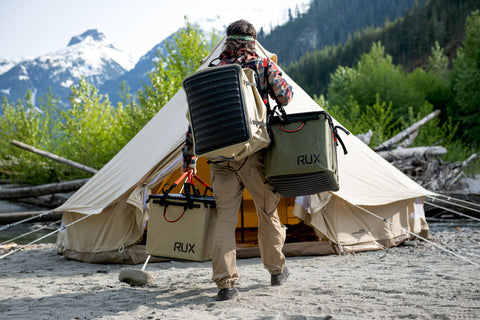 Man carrying multiple 70L Rux Bags to his tent. Holds all his gear.