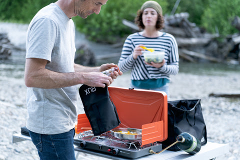 Friends cooking at their campsite. We see a man pulling out cooking spices from RUX Pocket to use for their BBQ.