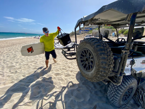 Man on the beach loading up his Jeep with his RUX gear after a big surf day.