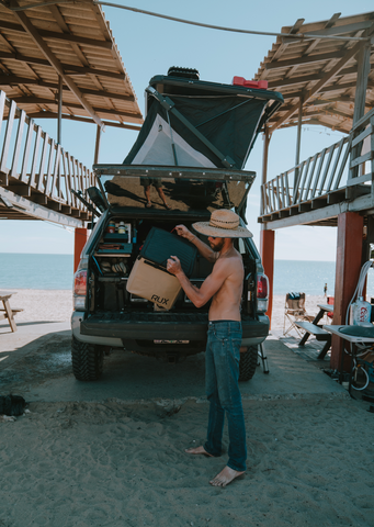 Man pulling out his RUX 70L from the back of his truck on a beach