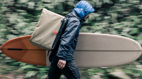 Man carrying his surfboard and wearing the RUX 70L as a backpack.