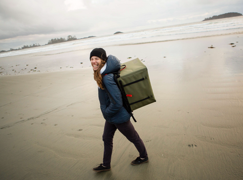 Girl walking on the beach in rainy weather smiling with her RUX 70L on her back.