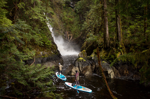 Two paddle boarders navigating towards a beautiful waterfall with their RUX bags beside them.