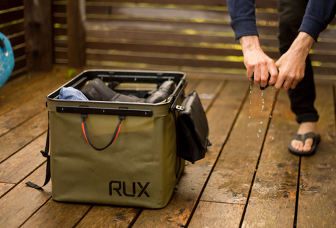 A close up shot of a man ringing water out from his sock and the RUX 70L bag next to him holding all of his boating gear.