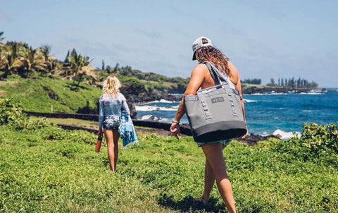 Women walking across a grassy walkway carrying their YETI 35L Carryall Tote.