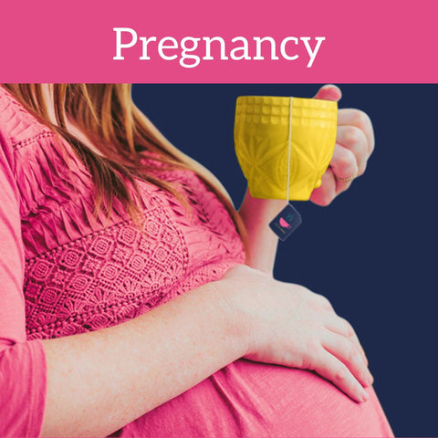 Pregnant lady in pink top drinking tea from yellow mug while touching baby bump