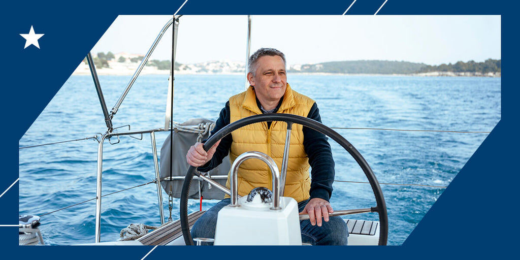 A father in a yellow jacket and jeans sitting at the helm of his boat and smiling.