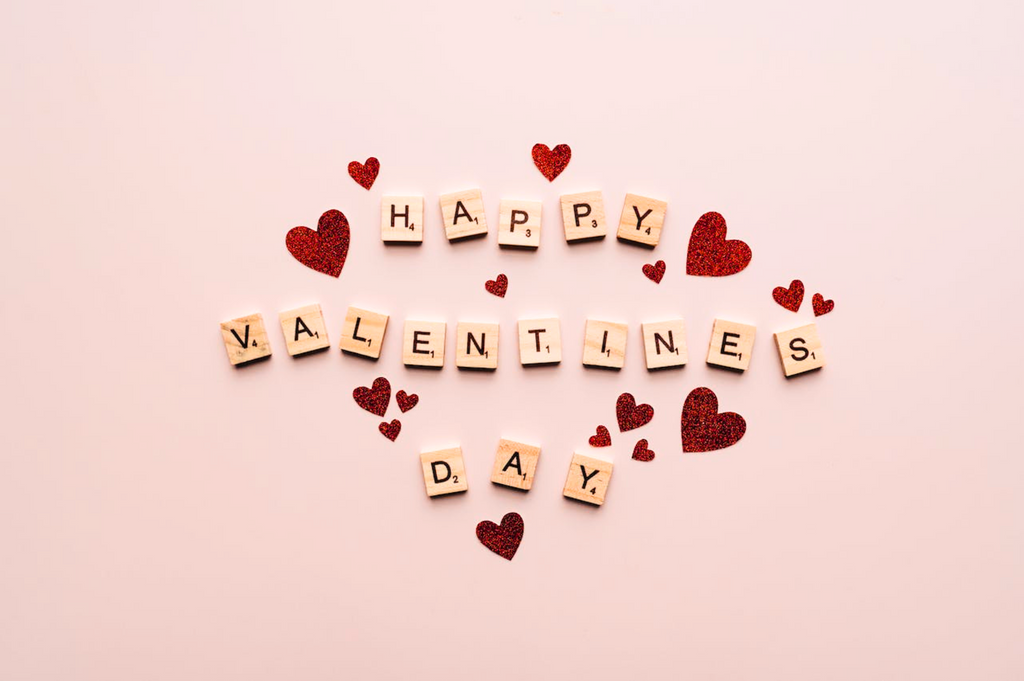 Scrabble letter tiles spelling out happy valentines day with red hearts surrounding letters