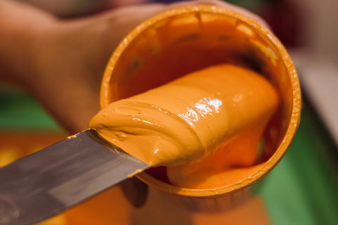 hands holding a container filled with yellow ink, spatula is scooping out some ink