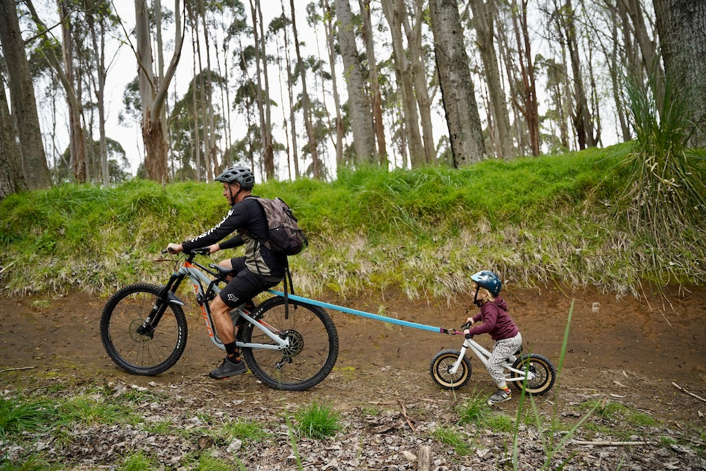Parent towing balance bike kid uphill using a mountain bike tow rope