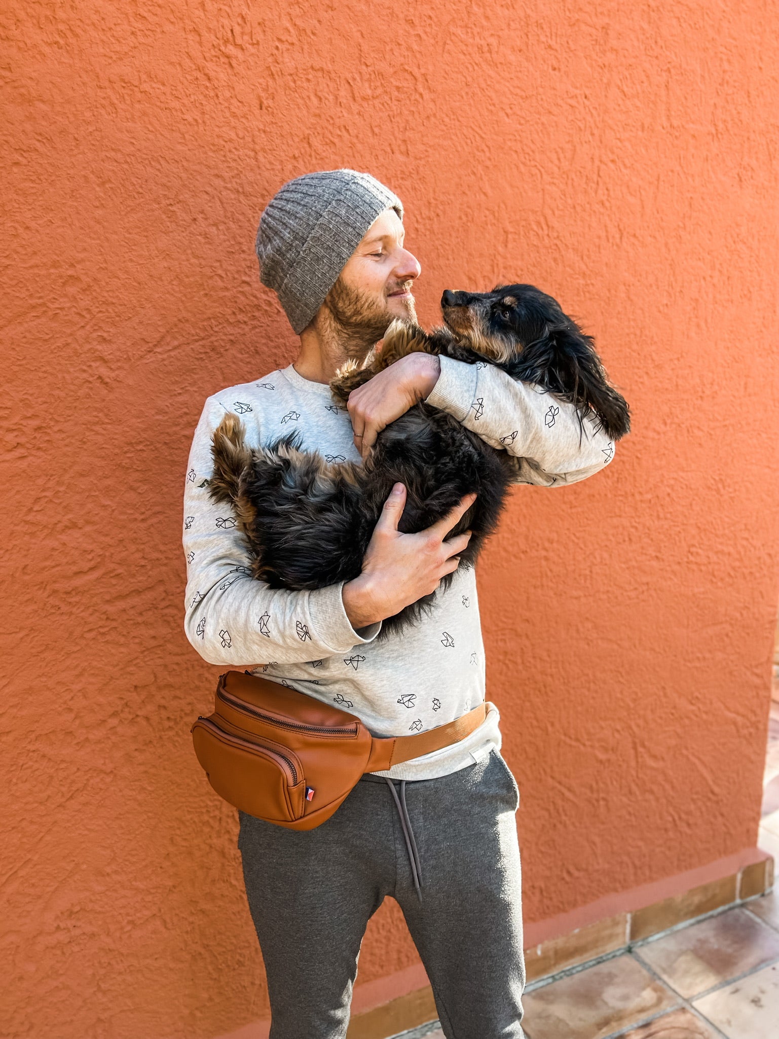 Man wearing dog walking bag fanny pack and lovingly holding his dog in his arms