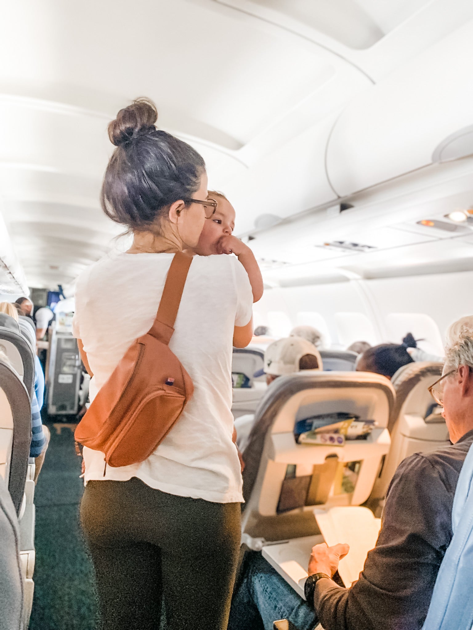 mom holding toddler on plane while standing in the aisle