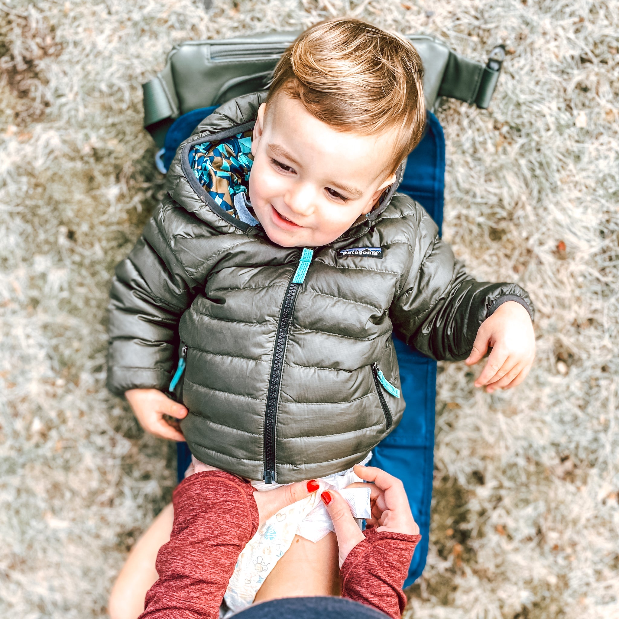 Mom changing toddler boy on changing pad on a hike