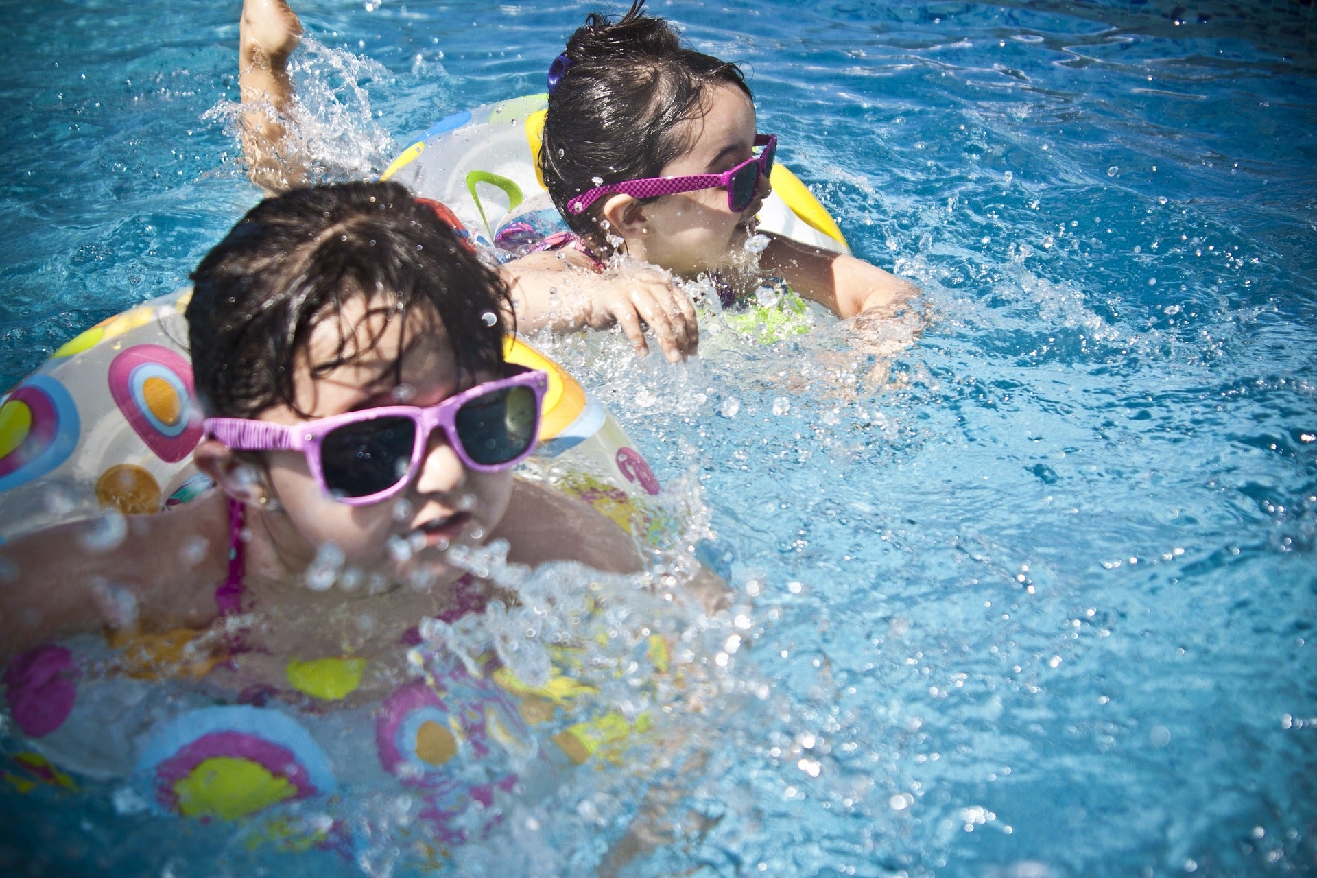 two toddler girls swimming in pool wearing sunglasses