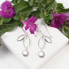 handmade silver two leaf earrings with coin pearl dangles on white background with flower accent