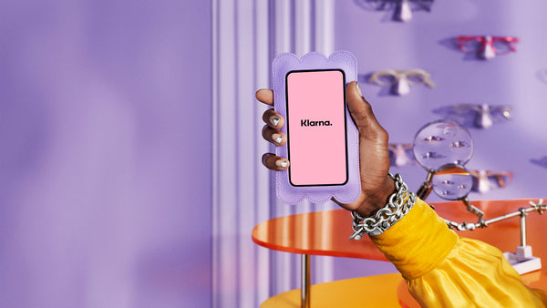 Buy now pay later with Klarna. Image is of a woman's hand holding up a phone screen with the Klarna logo in pink and black.