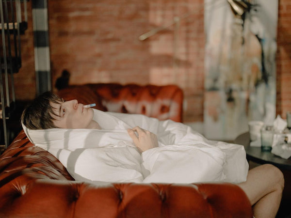 A sick man lying down in bed covered in a bed sheet