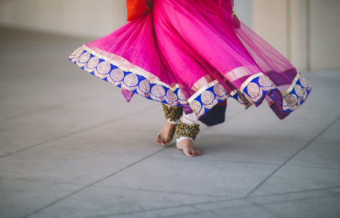 Photo of a woman's feet, with a flowing pink dress that has a blue trim. Photo by Saksham Gangwar on Unsplash