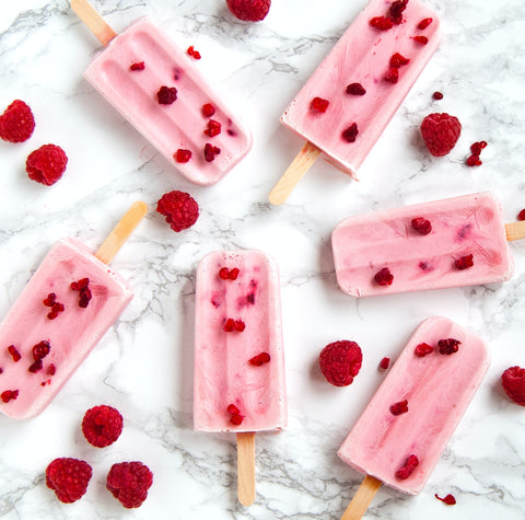 Pink raspberry popsicles are scattered on a marble countertop with other fresh raspberries. Photo by Daniel Oberg on Unsplash