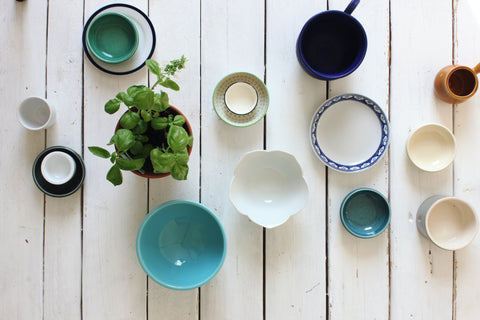 Top down view of a tabletop with a scattered assortment of  bowls, cups, mugs, and one plant on it. Photo by Angele Kamp on Unsplash.